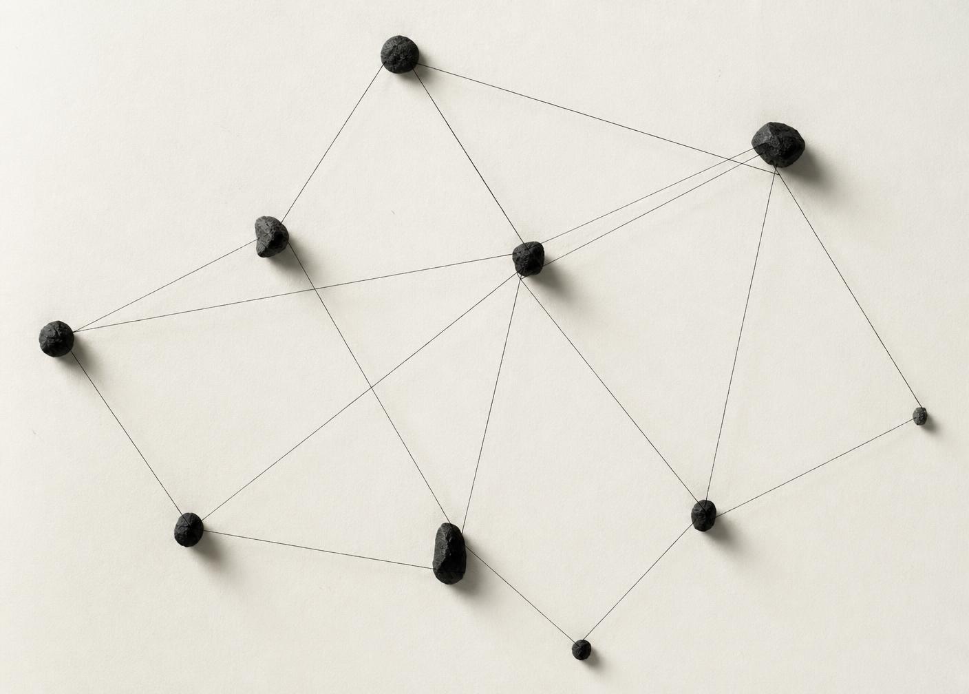 Dark stones connected by fine threads on pale paper, representing the systemic dynamics of an organisation